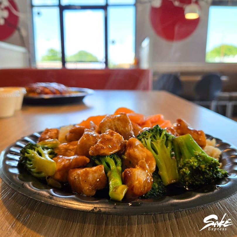 Sake Express's Japanese chicken and broccoli dish with rice and carrots on a black plate.