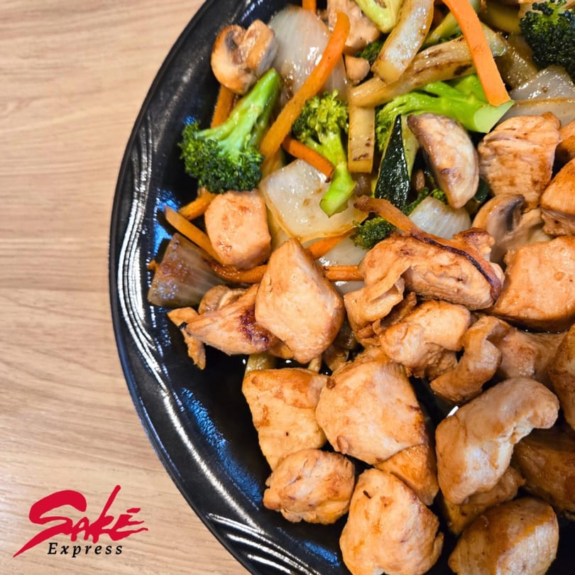 Sake Express chicken and vegetable stir-fry with broccoli, carrots, onions, and mushrooms on a black plate.