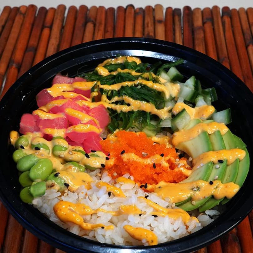 Sake Express poke bowl with tuna, edamame, avocado, roe, seaweed, and rice, drizzled with sauce.