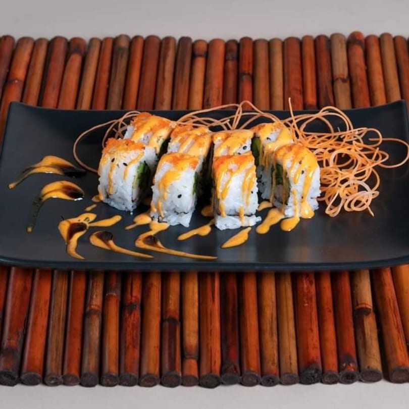 Sake Express sushi rolls with orange sauce and crispy noodles on a black plate.