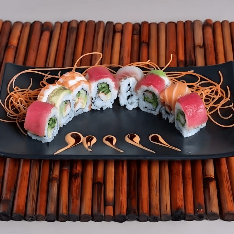 Assorted sushi rolls with tuna, salmon, and avocado on a black plate with carrot garnish.
